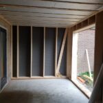 Aanbouw in houtskeletbouw tegen een stenen woning, met houten stijlen en dampopen folie